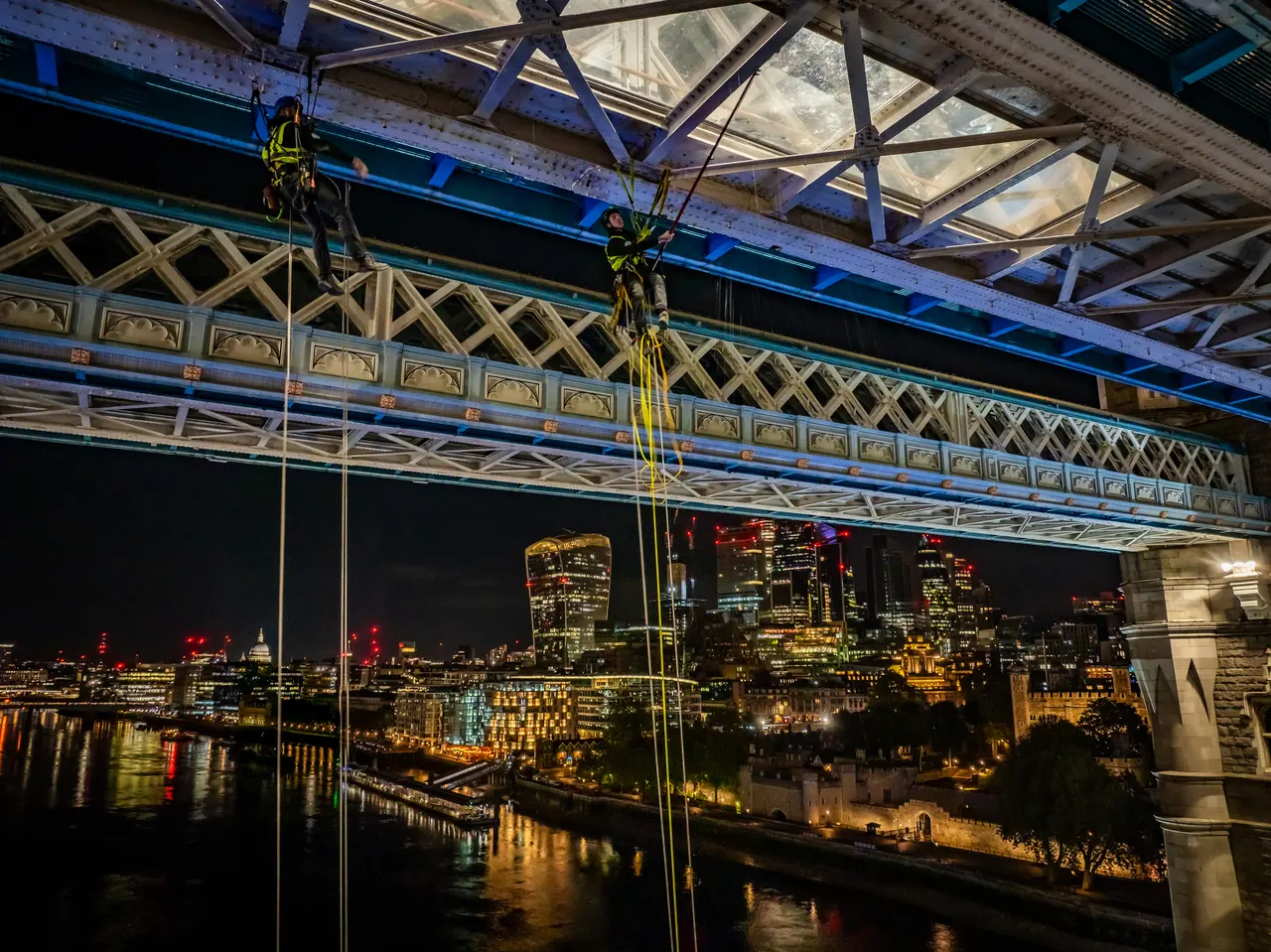 Rope-access specialists suspended beneath Tower Bridge’s glass walkways above the Thames at night